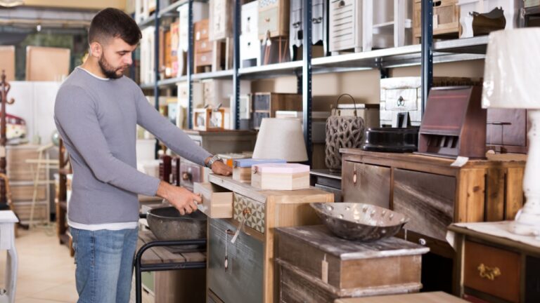 Portrait of handsome male choosing small cabinet in shop of secondhand furniture