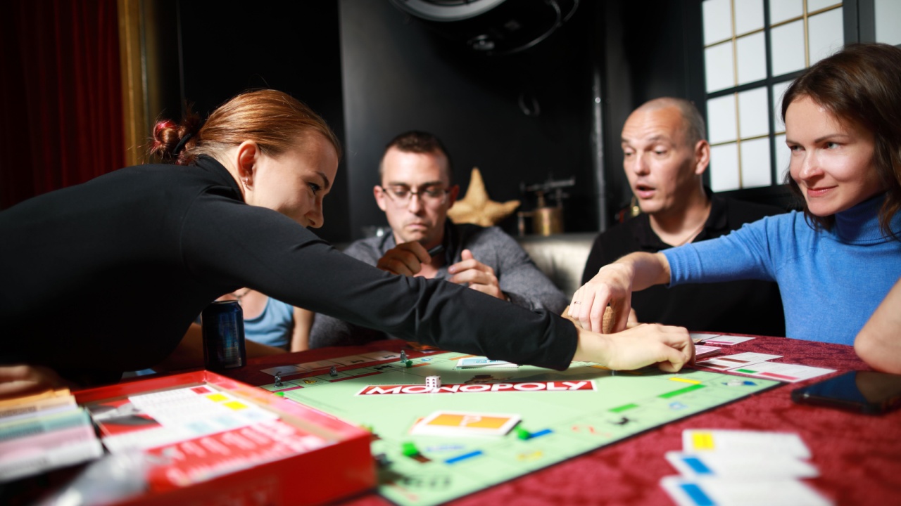 5 September 2019:Group of people playing Monopoly board game together at night.Friends with funny emotions enjoying the game in evening
