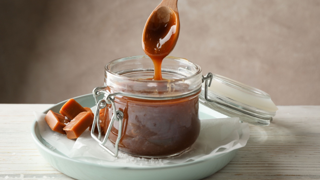 Glass jar with salted caramel and candies on wooden background, space for text