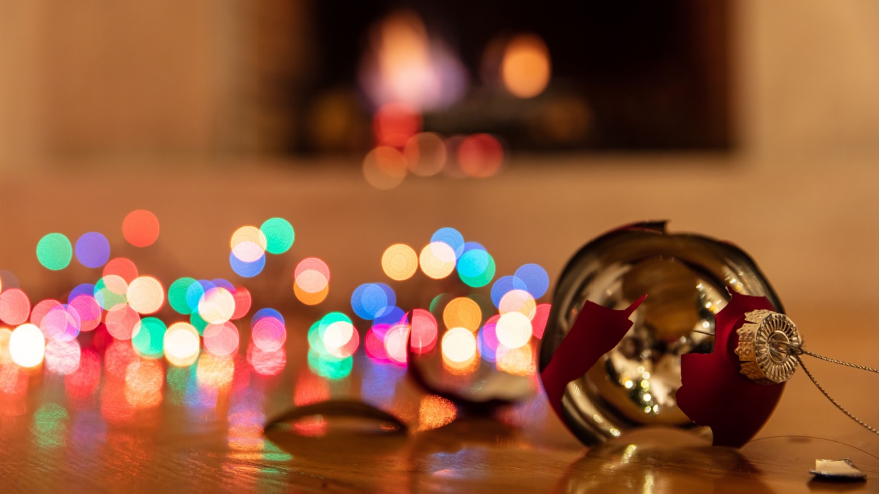 Christmas ornament broken. Xmas holiday decoration, lights glowing, blur burning fireplace background, reflections on the wood floor