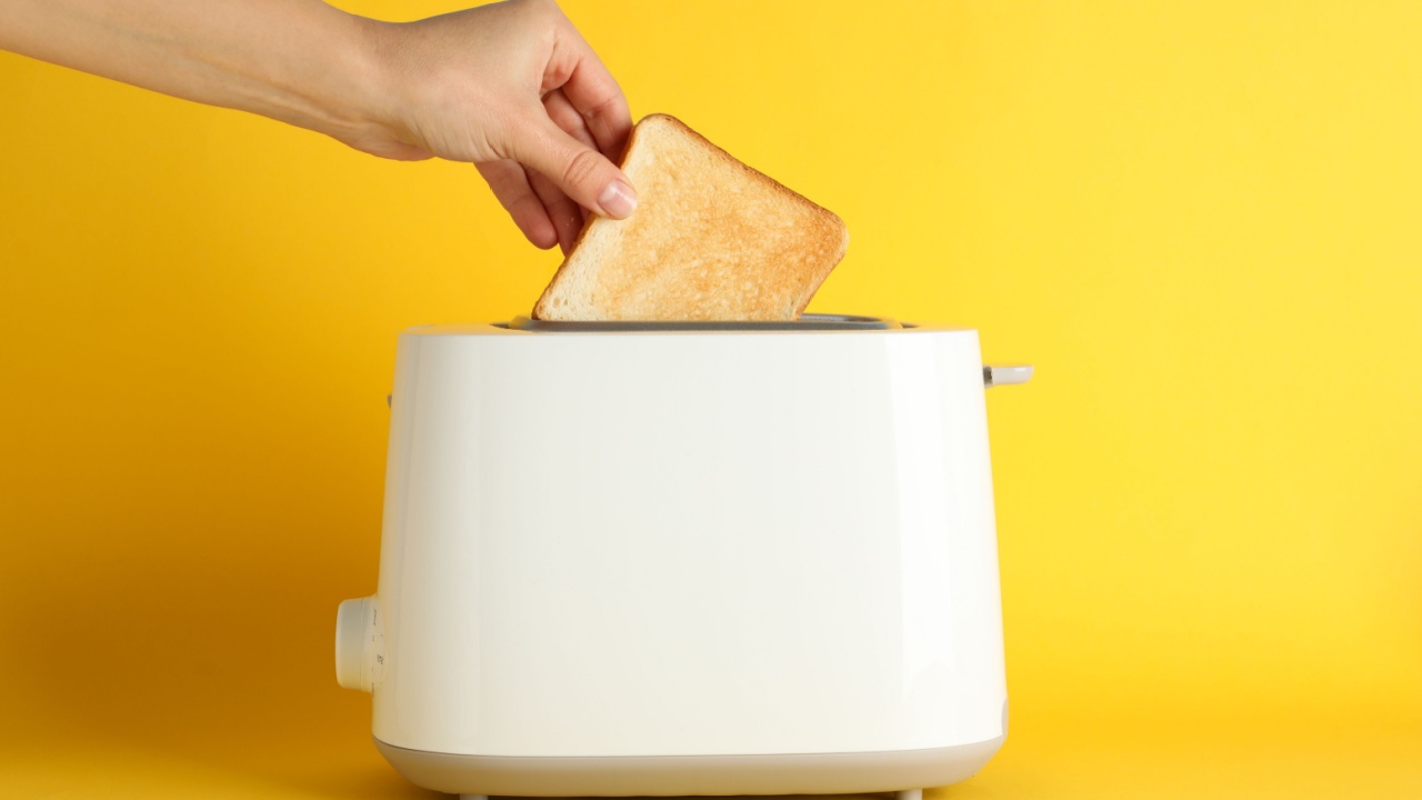Female hand puts bread in a toaster on yellow background, space for text