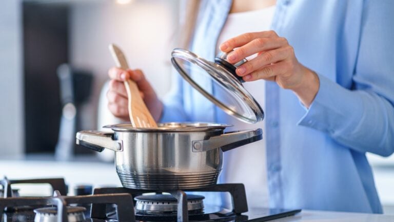 Woman housewife using steel metallic saucepan for preparing dinner in the kitchen at home. Kitchenware for cooking gas stove