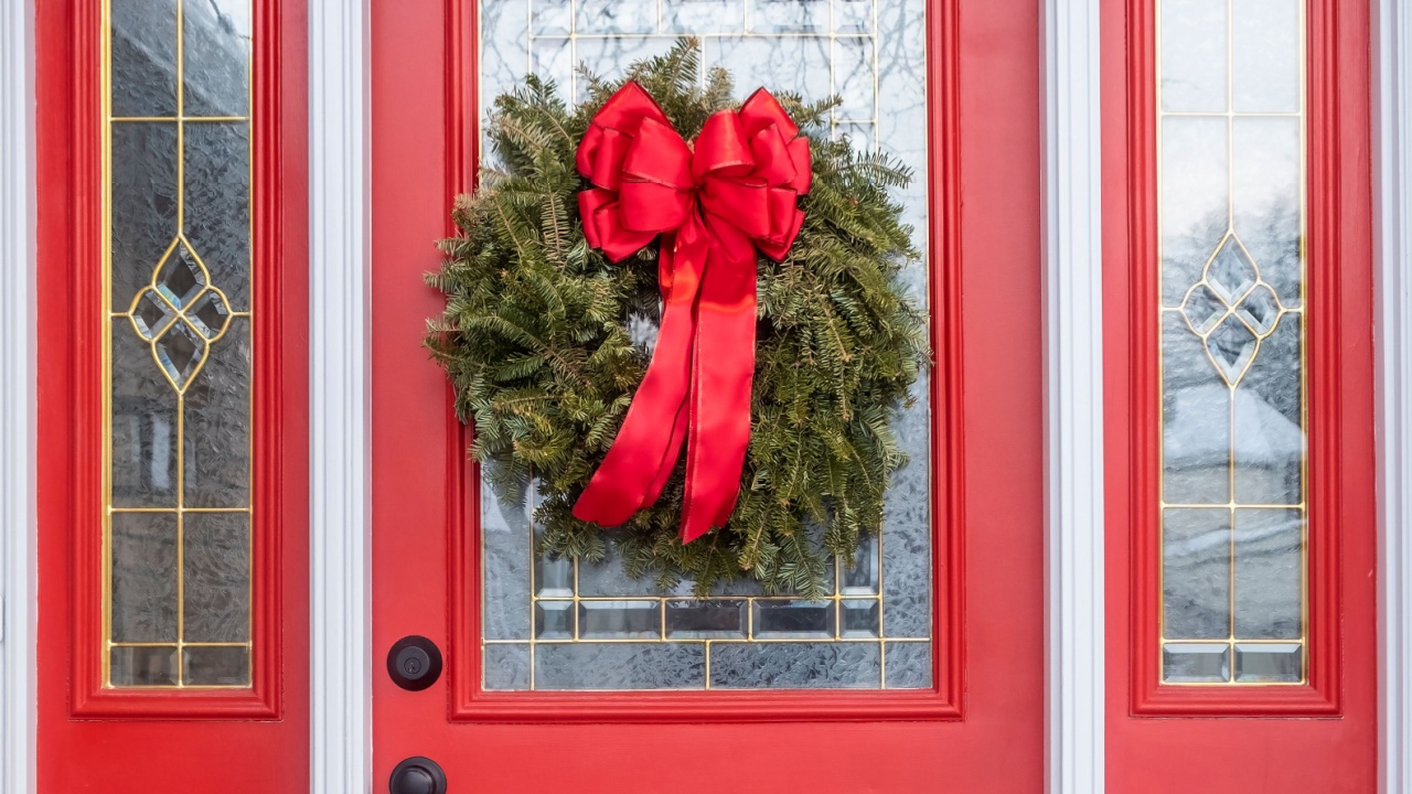 Red House Door Decorated with a Real Pine Christmas Wreath and a Big Red Satin Bow