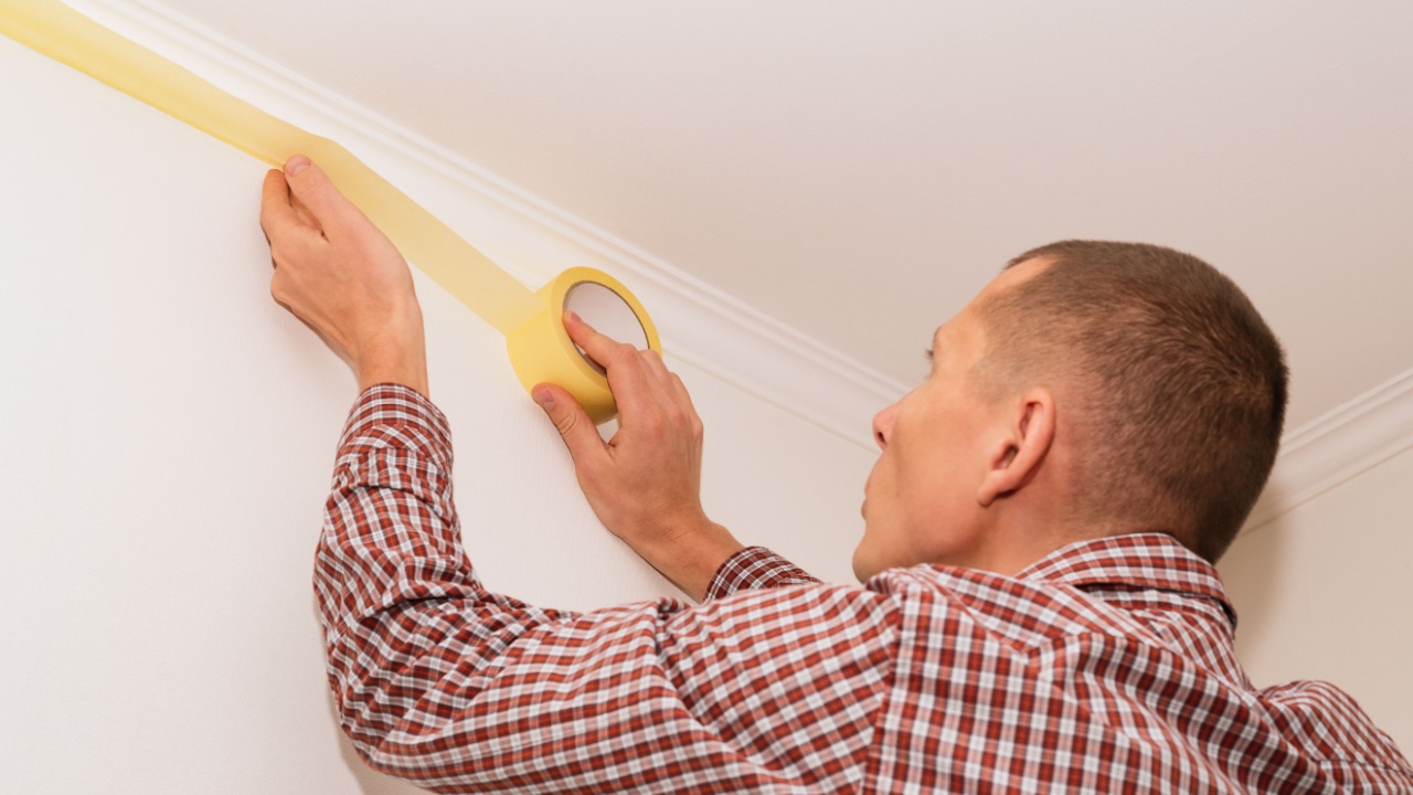 Home repairman prepares walls for painting. Masking ceiling masking tape