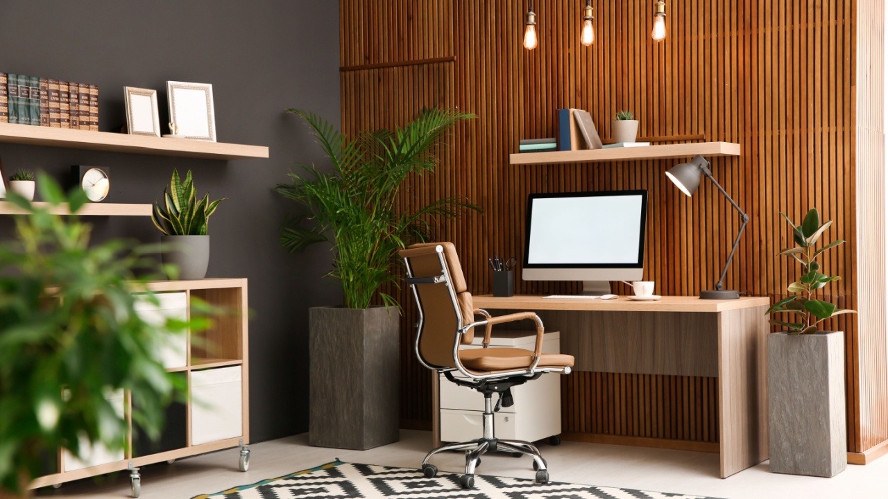 Comfortable workplace with computer near wooden wall in stylish room interior. Home office design
