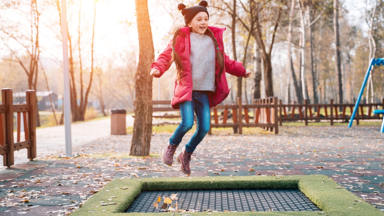 Happy school girl jumping on a small trampoline in the park