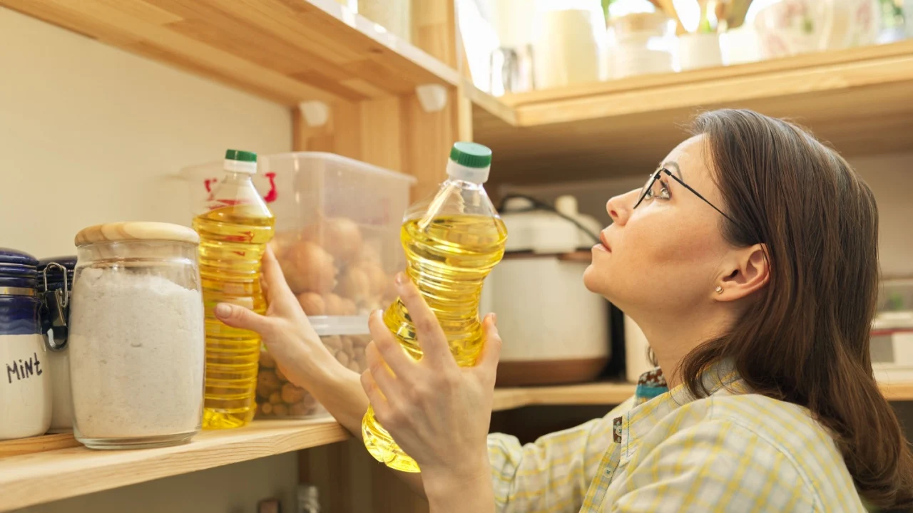 Food storage, wooden shelf in pantry with products. Woman taking food, sunflower oil for cooking.