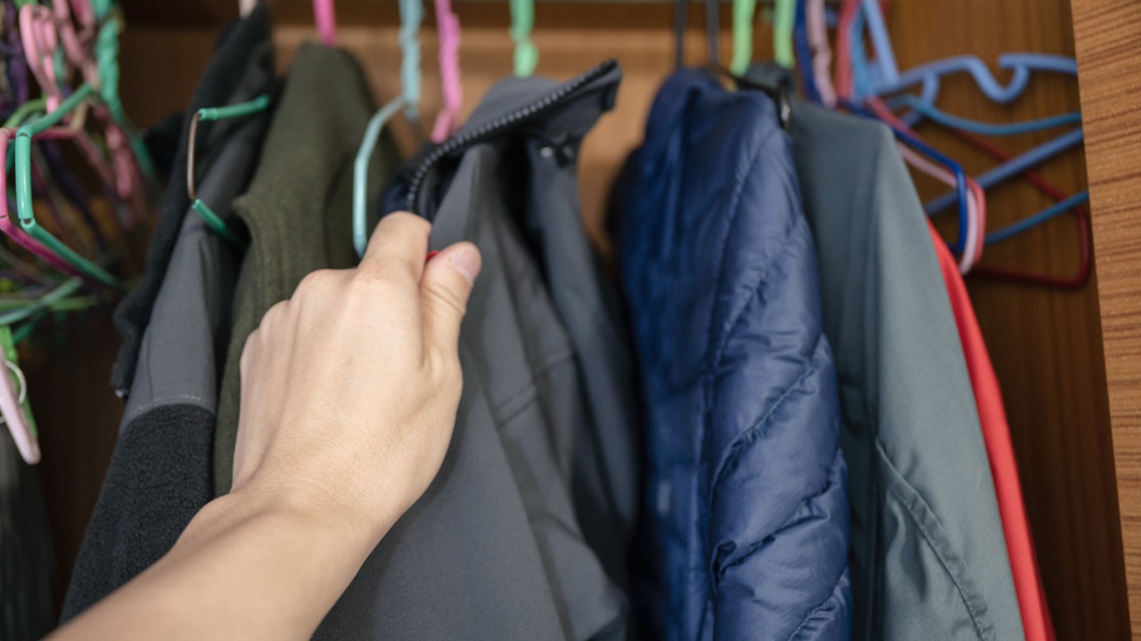 Hand choosing winter jacket on clothes rack in wood closet