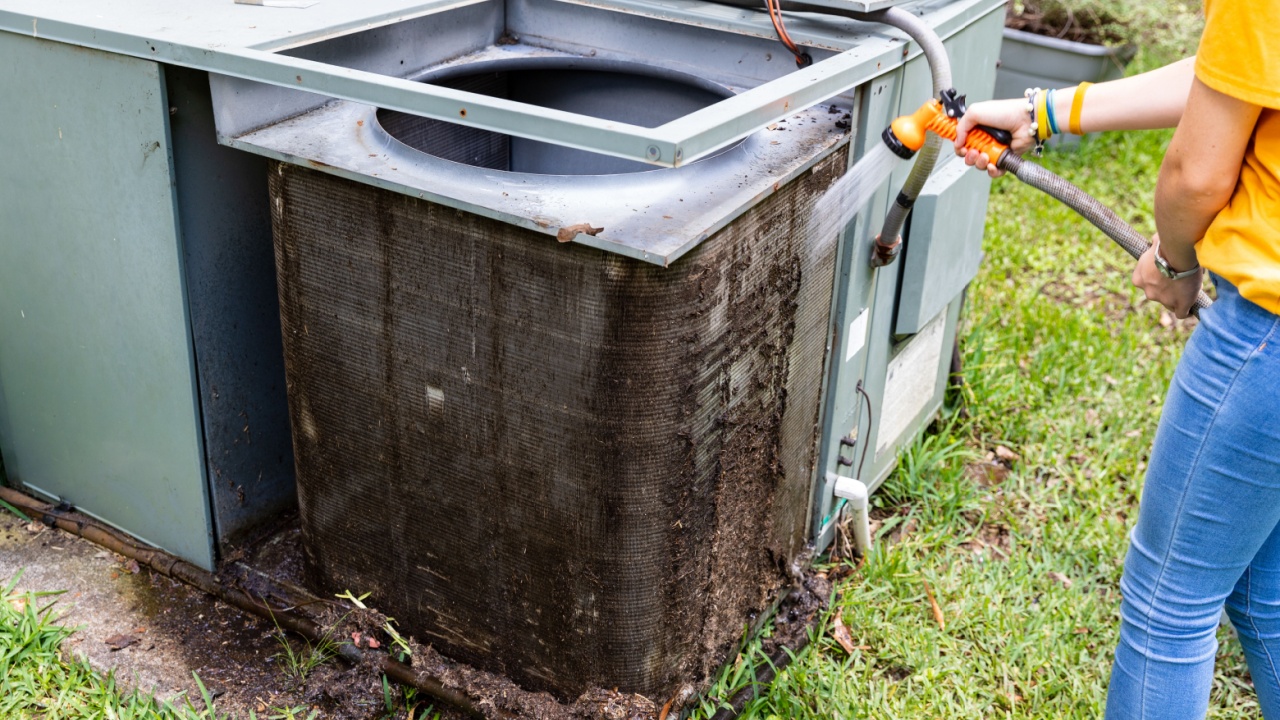 Person cleaning dirty condenser coils on an air conditioner system