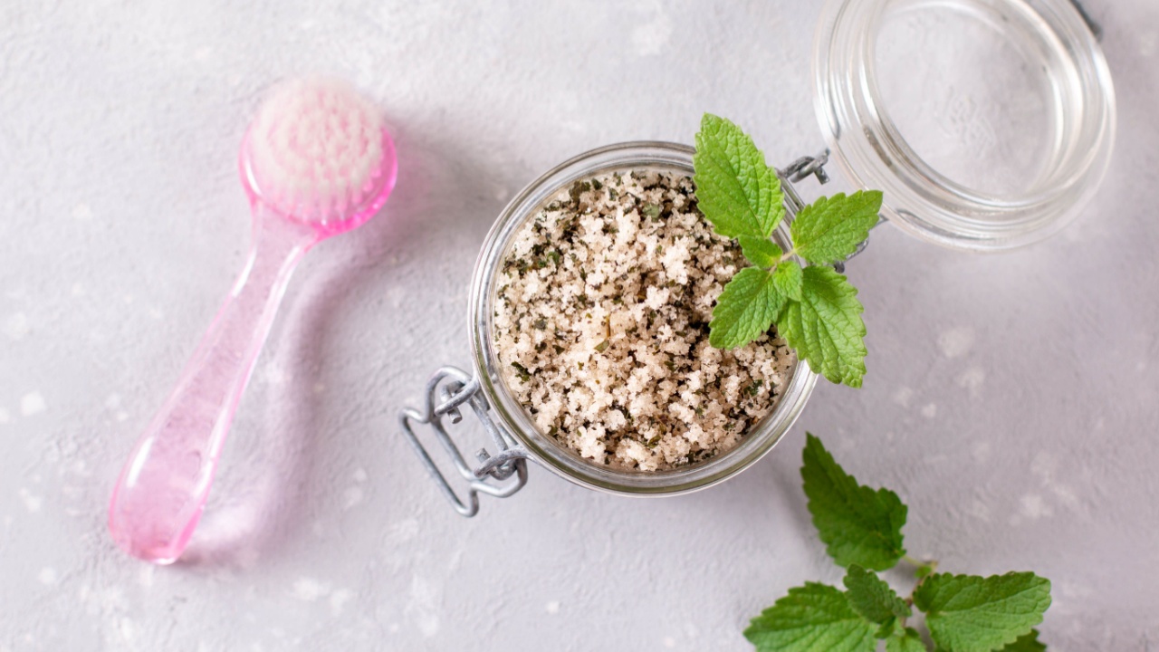 Homemade sugar scrub with chopped mint leaves and body brush on a light background. Natural beauty treatments