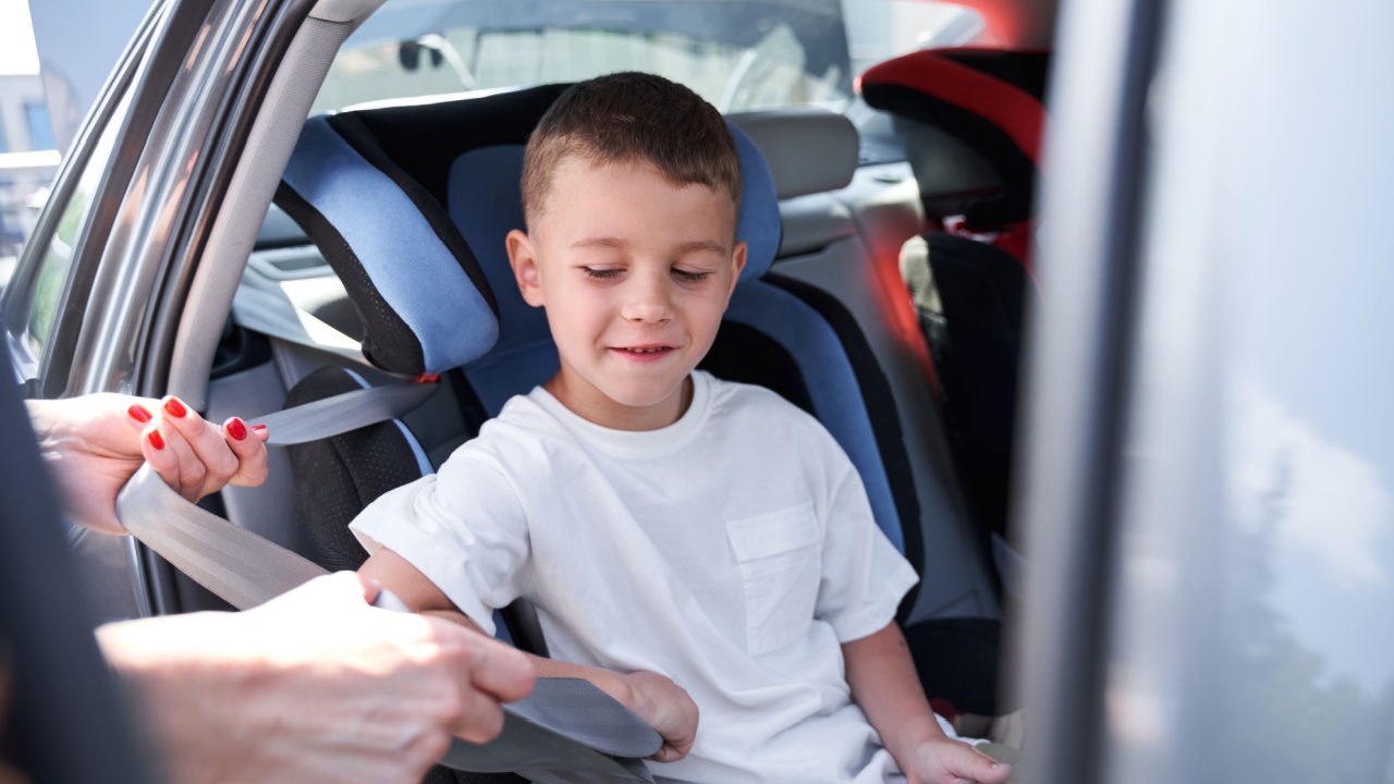 Happy boy is sitting in child chair in car while mom is taking care of his safety on road