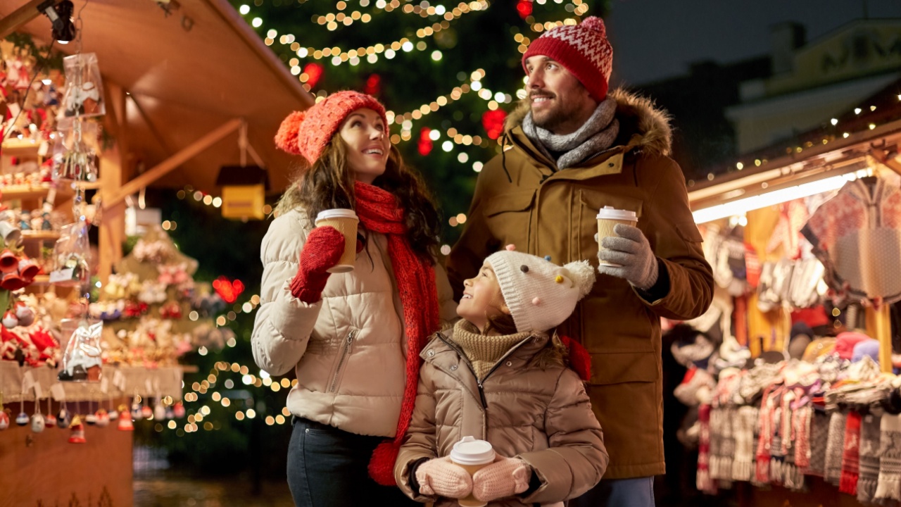 family, winter holidays and celebration concept - happy mother, father and little daughter with takeaway drinks at christmas market on town hall square in tallinn, estonia