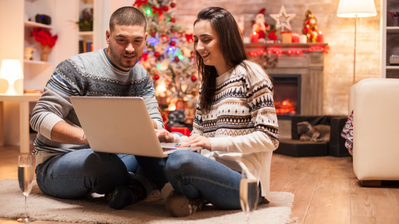 Relaxed couple on christmas day in front of fireplace smiling while using laptop.