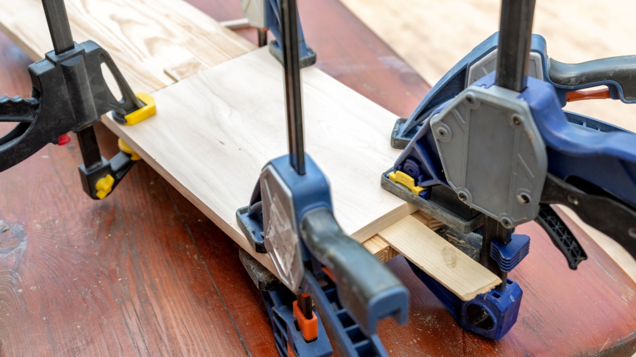 Joining wooden handmade box with clamps joiners after glueing. Different chisels, drills and pencils at craftsman workshop. DIY instruments on wood workbench. Workplace organization arrangement