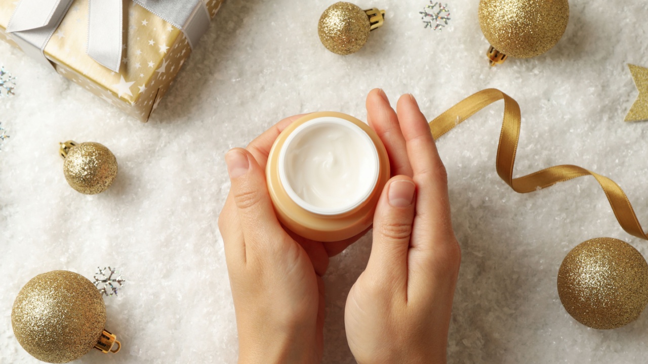 Female hands hold jar of cosmetic cream on background with Christmas accessories