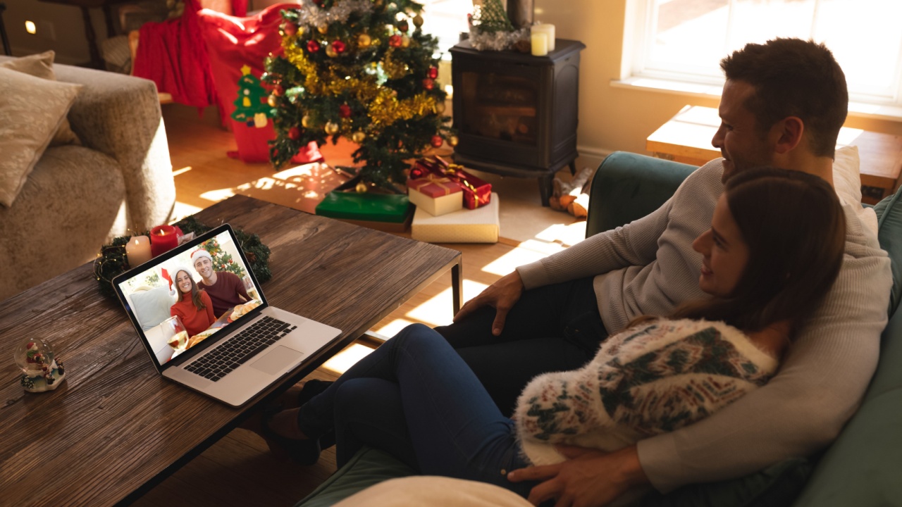 Couple sitting on couch having a videocall with couple in santa hats smiling on laptop at home. social distancing during christmas festivity quarantine lockdown concept.