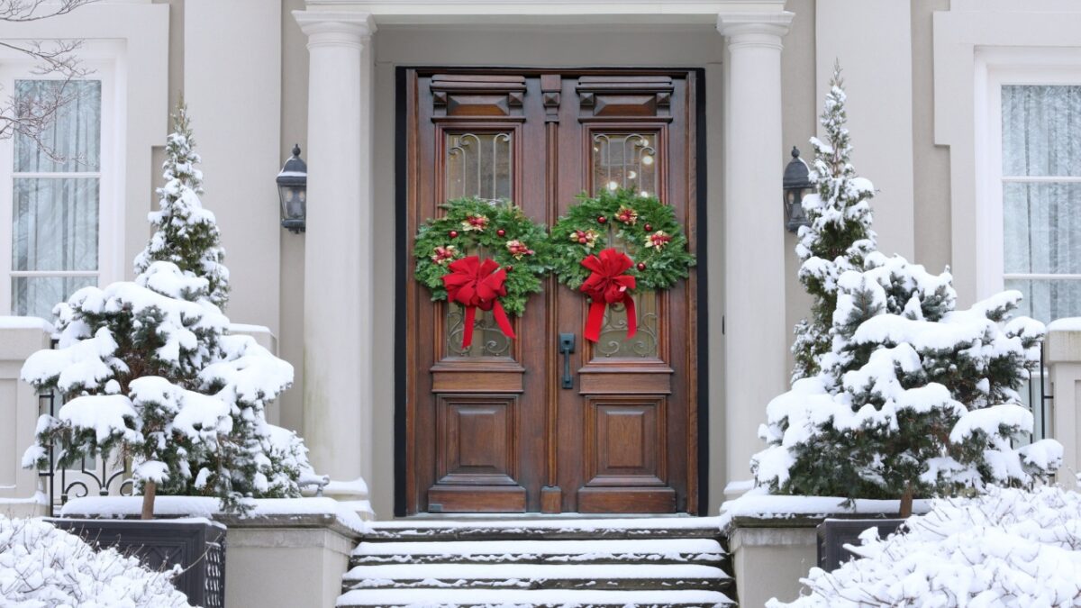 Front door of stucco house with colorful Christmas wreath and elegant wooden double door