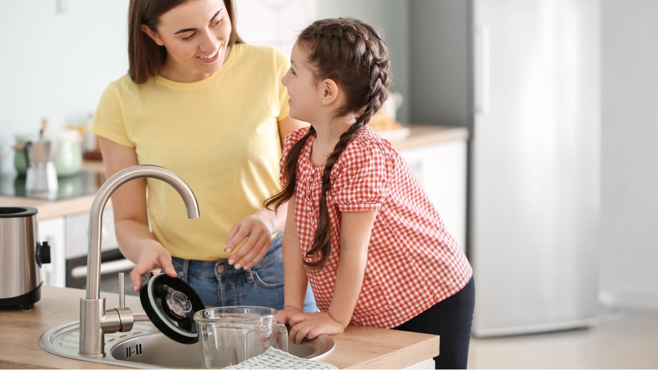 Mother and little daughter cleaning blender in kitchen