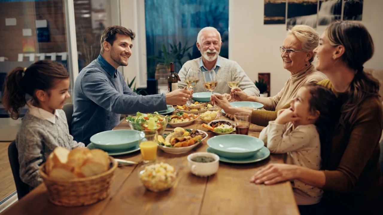 Happy multi-generation family toasting with wine during a meal in dining room.