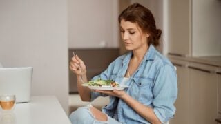 Pleased woman crossing legs while enjoying her meal, being in the kitchen