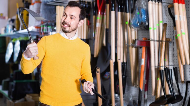 Young smiling cheerful positive man choosing various tools in garden equipment shop