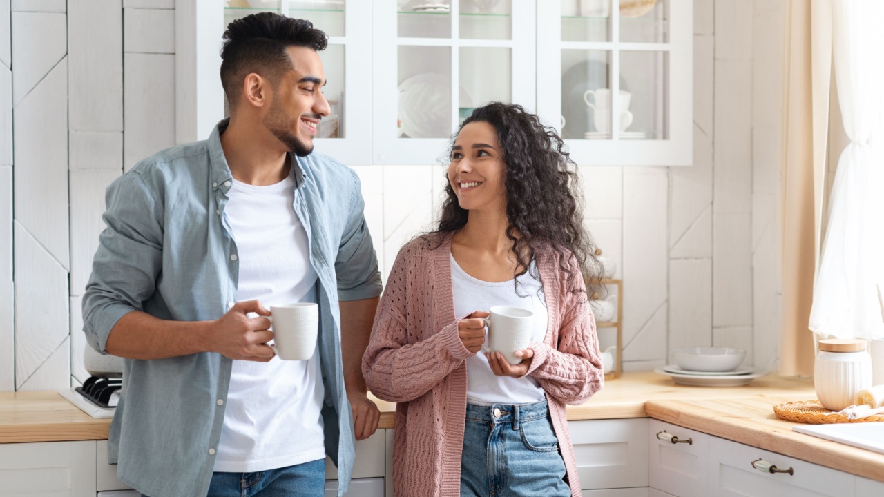 Portrait Of Romantic Young Arab Spouses Drinking Morning Coffee In Kitchen, Millennial Middle Eastern Man And Woman Enjoying Hot Drinks And Smiling To Each Other, Spending Time At Home Together