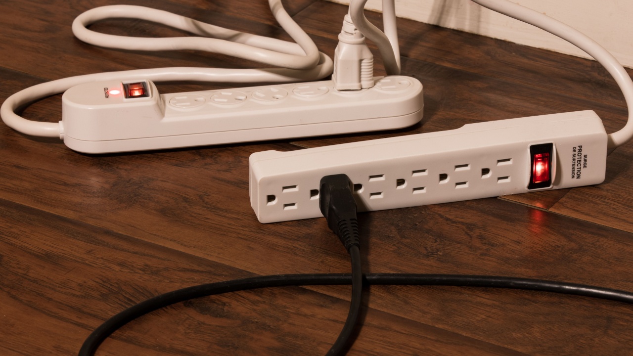 A black power cord plugged into a surge protector which is plugged into another extension cord. Known as daisy stripping, this usage of power strips is a fire hazard and is highly dangerous.