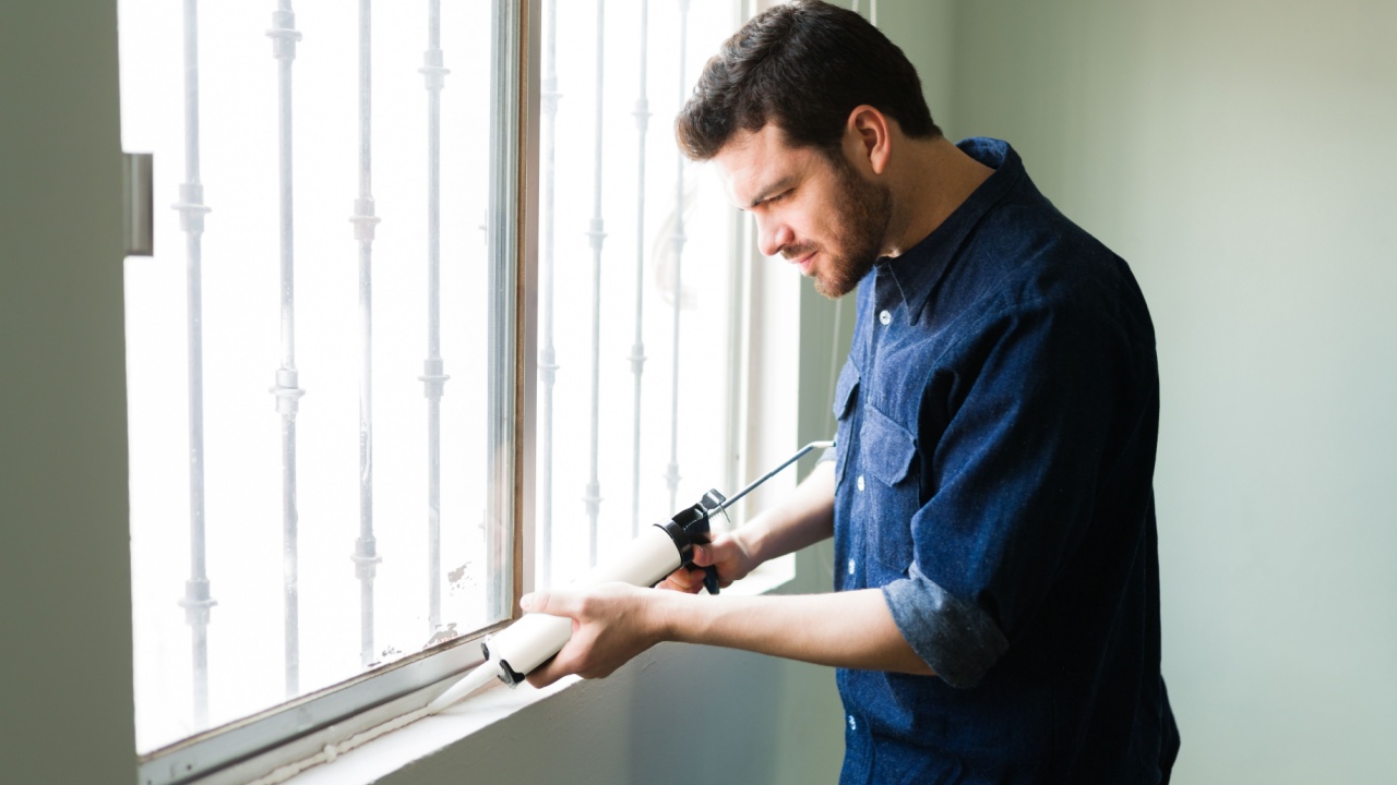 Attractive young man and handyman insulating his home windows during the winter season