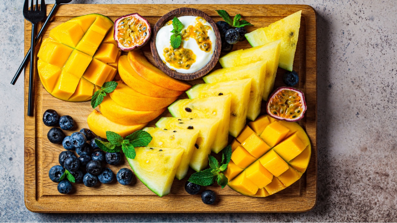 Tropical fruit charcuterie dessert grazing platter on wooden board, dark background, top view.