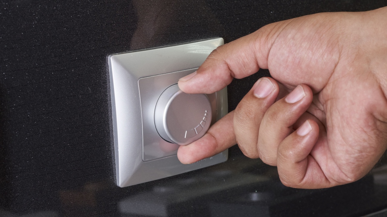 Human hand turning down electrical light dimmer switch or conditioner heat controller - saving energy concept