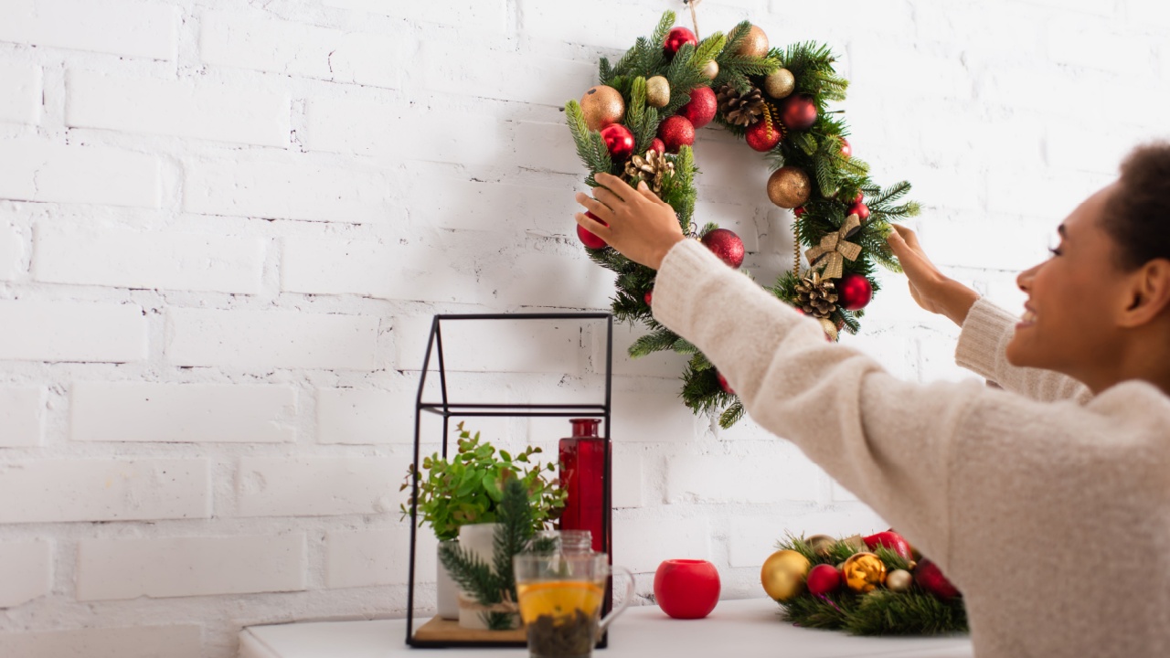 Smiling african american woman holding christmas wreath near fireplace and tea