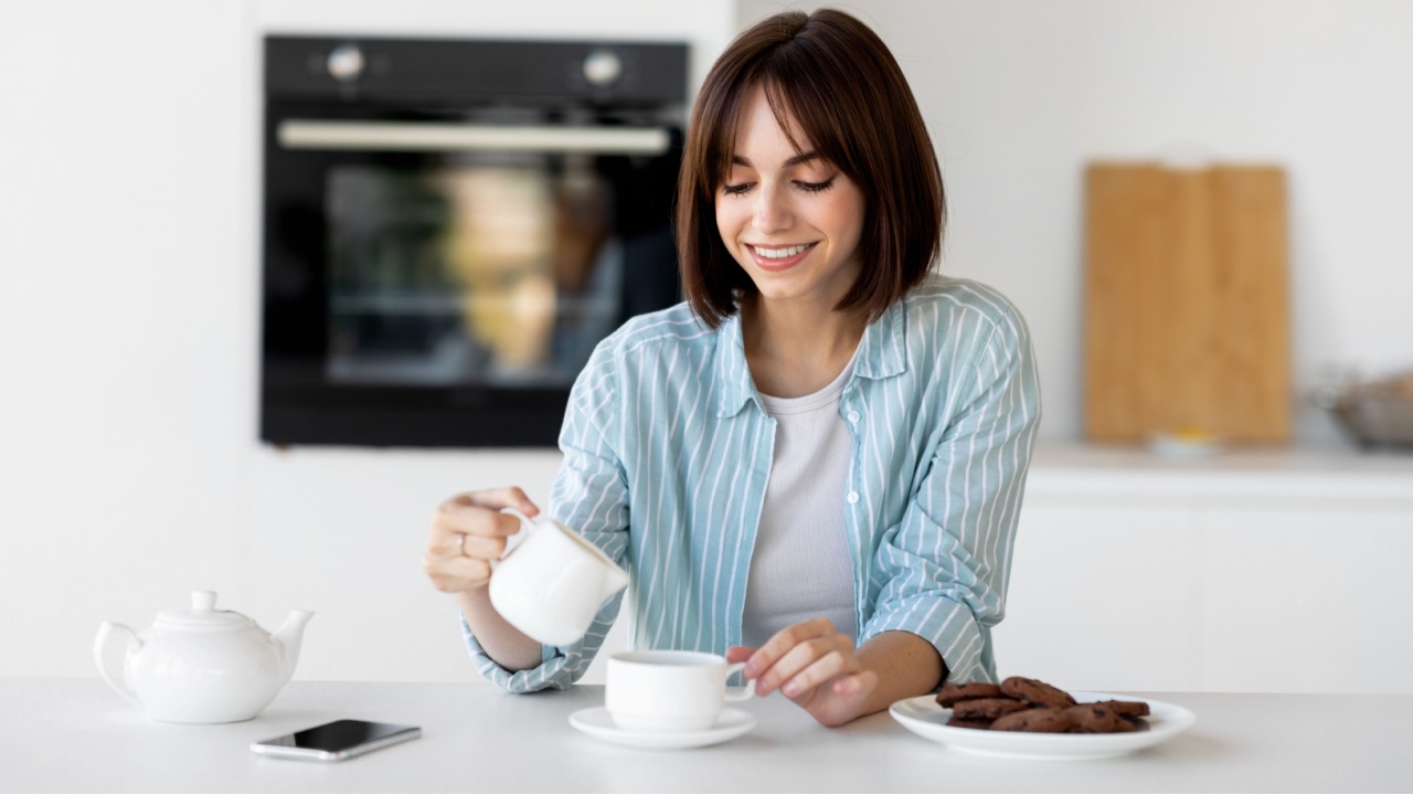 Happy young lady pouring milk in cup of coffee, sitting in kitchen interior, enjoying morning hot beverage and start of new day, empty space