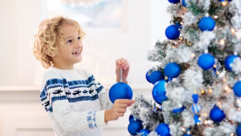 Child decorating Christmas at home. Opening gifts and presents on Christmas morning. Blue and white Xmas decoration theme. Little kid in sweater with ornament. Family celebrating winter holidays.