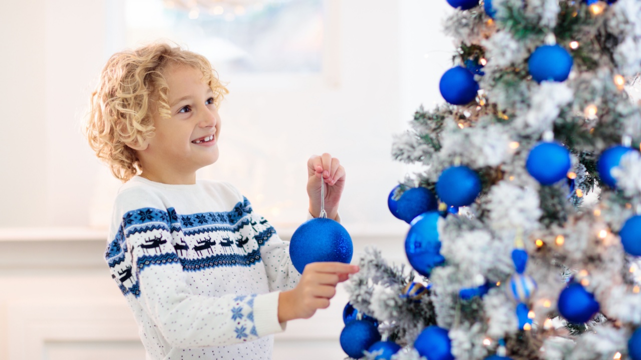 Child decorating Christmas at home. Opening gifts and presents on Christmas morning. Blue and white Xmas decoration theme. Little kid in sweater with ornament. Family celebrating winter holidays.