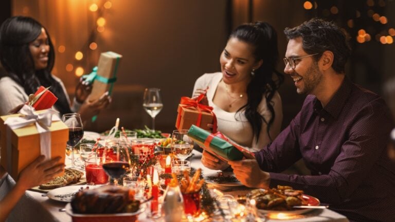 holidays, party and celebration concept - multiethnic group of happy friends having christmas dinner and giving presents at home