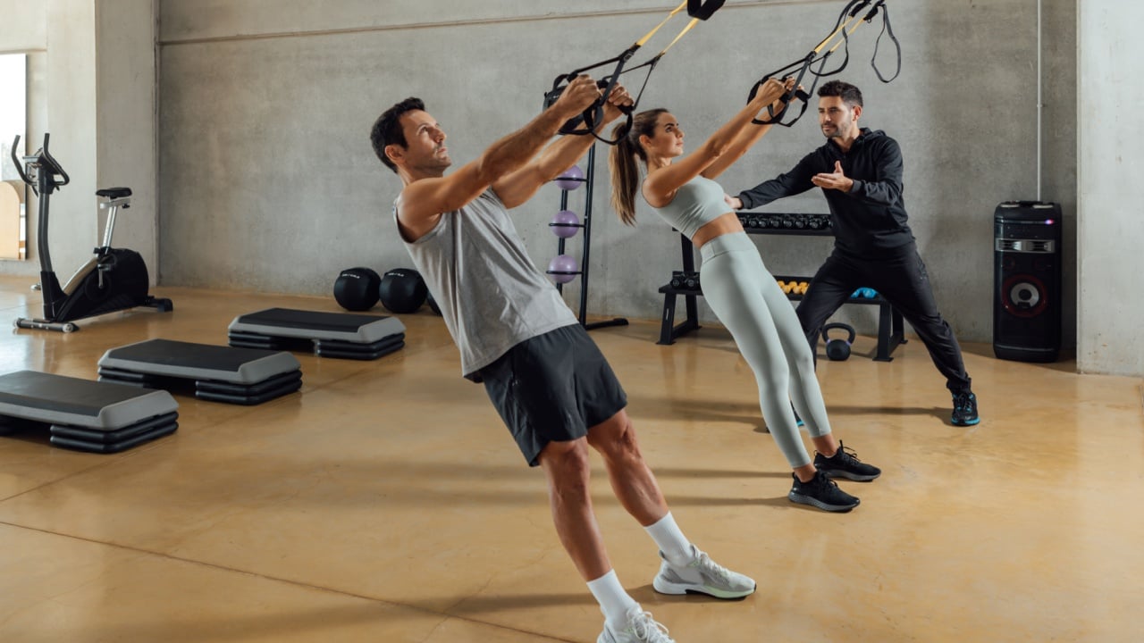 Personal trainer assists a couple that work out with elastic resistant strap.