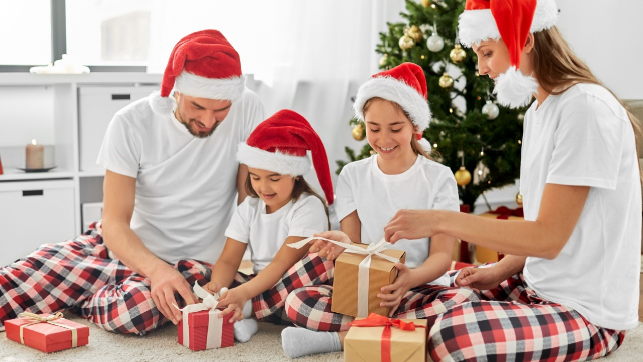 family, winter holidays and people concept - happy mother, father and two daughters in santa hats opening christmas gifts at home