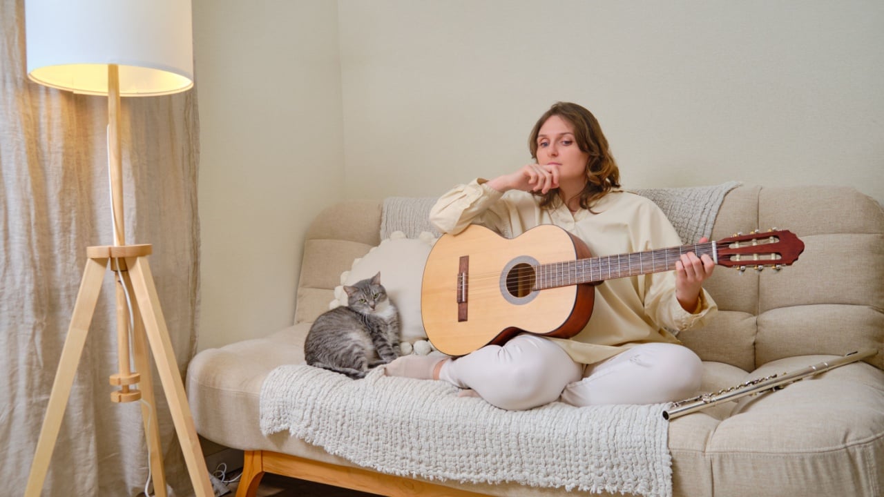 Sad woman musician playing guitar at home on sofa in living room