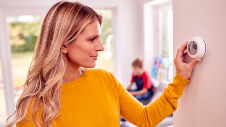 Mother At Home With Son Adjusting Smart Central Heating Thermostat Control