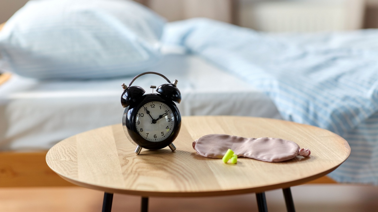bedtime and morning concept - close up of alarm clock, earplugs and eye sleeping mask on night table at home