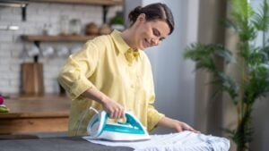 Smiling beautiful housewife ironing the wrinkled shirt