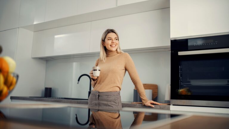 A happy woman drinking coffee at her modern kitchen.