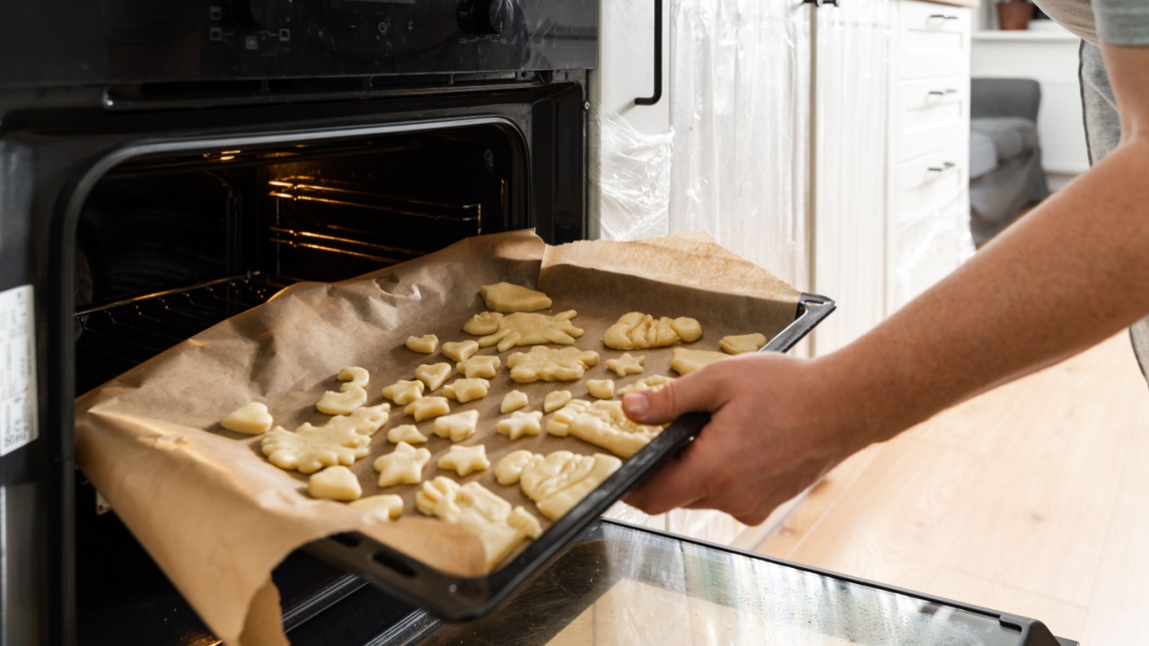 Close up view of the male person in apron standing in front of the open oven and putting pastry on the sheet pan into it. Stock photo