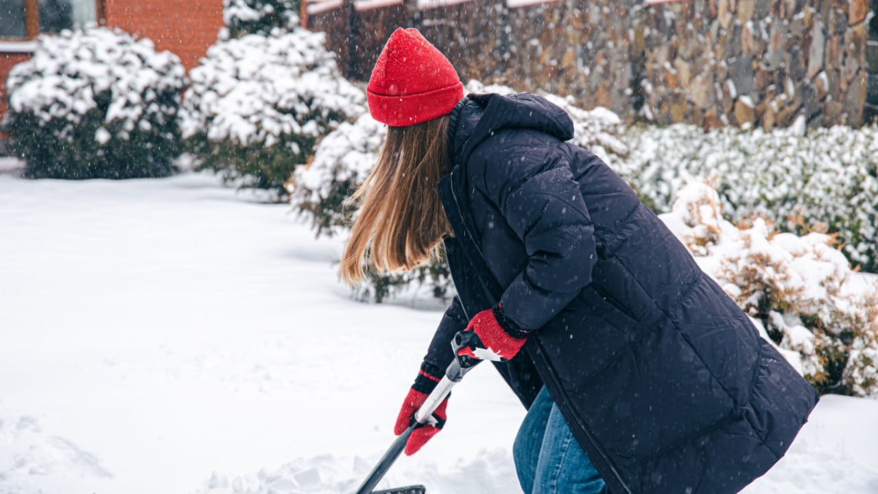 Young woman cleans snow in the yard in snowy weather.