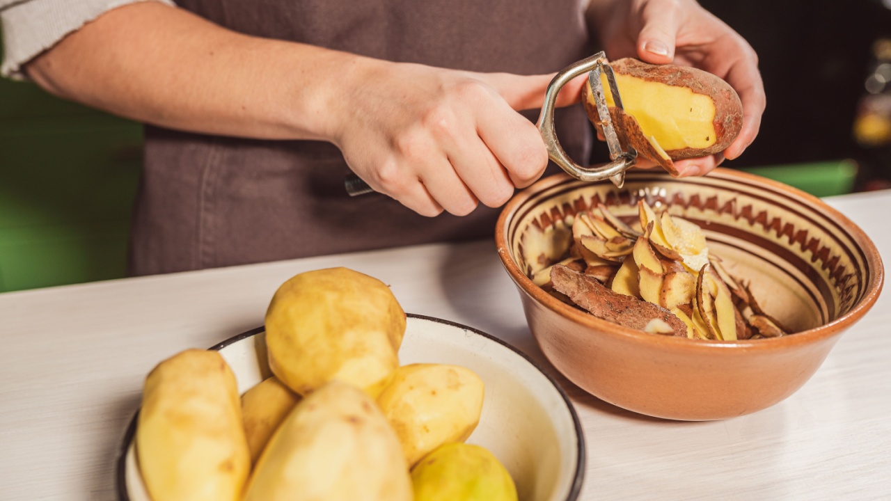 hands of cook cut peel of raw potatoes with kitchen knife for peeling vegetables, peeler, put food waste in separate container for further processing. Zero waste, using organic waste for compost