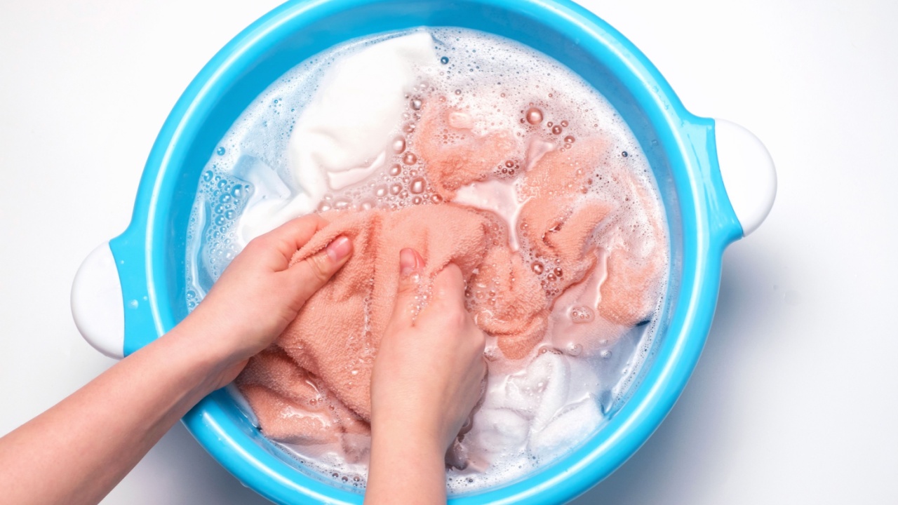 Female hands washing multicolored towels in basin, top view.