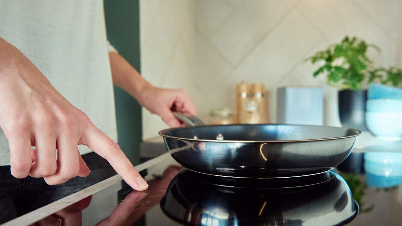 Modern kitchen appliance, Woman hand turn on induction stove with steel frying pan, Finger touching sensor button on induction or electrical hob
