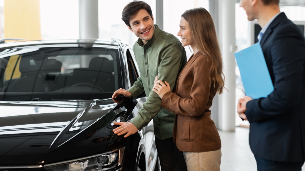 Car purchase or rental. Millennial Caucasian couple speaking to salesman about buying new automobile at dealership. Confident young manager showing customers choice of autos at salon