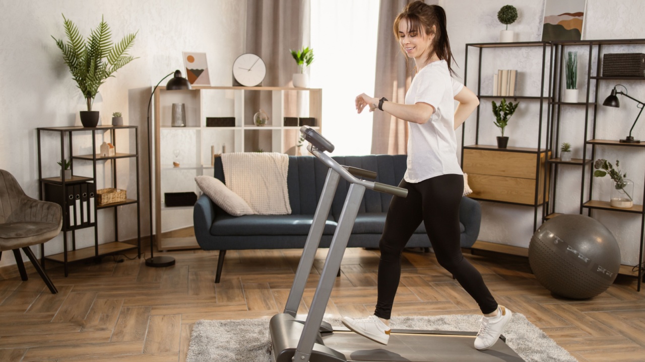 Beautiful caucasian women with long black and tied hair in a sports leggings and a white T-shirt and sneakers doing exercise by running on the electric treadmill in the fitness room .