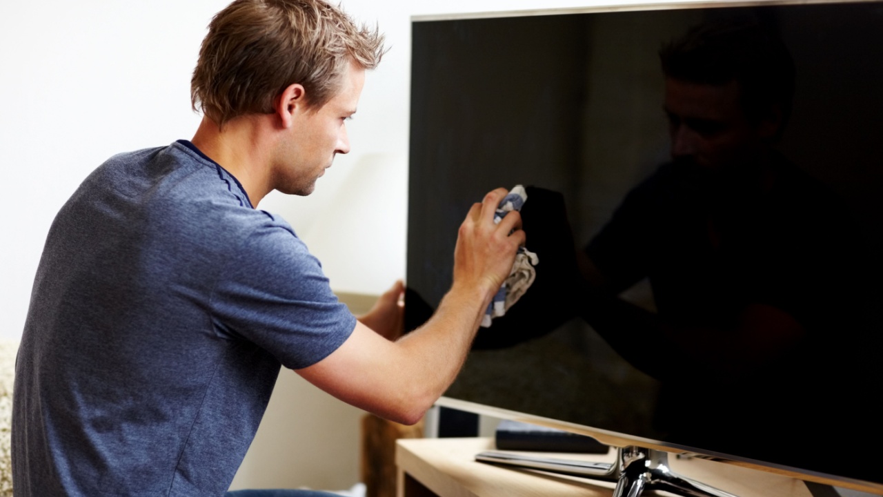 Taking care of his electronics. Young man cleaning the screen of his smart TV.